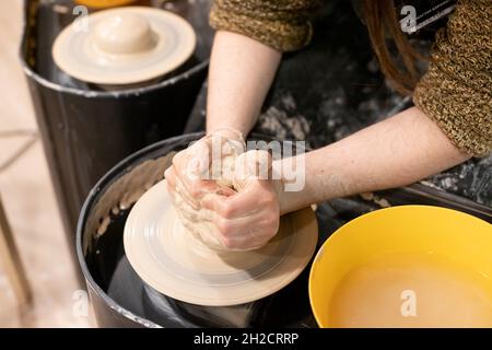 Un primo piano di una donna vasaio insegna una donna come modellare correttamente una ciotola di argilla marrone sulla ruota di un vasaio Foto Stock