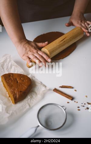 Le mani femminili stendono l'impasto allo zenzero crudo con un matterello su una tovaglia bianca Foto Stock