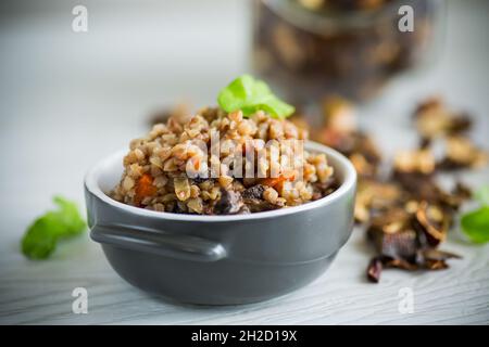grano saraceno bollito con verdure e funghi secchi della foresta in uno stampo di ceramica su un tavolo di legno Foto Stock