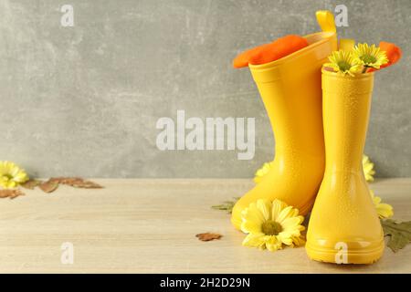 Stivali di gomma con fiori su tavola di legno con foglie. Foto Stock