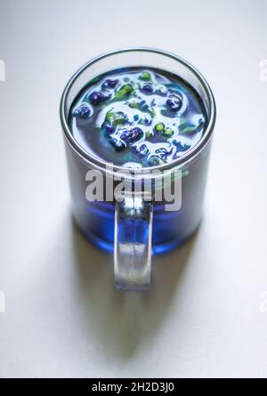 Una tazza di vetro trasparente di tè di piselli blu Butterfly su sfondo bianco. Foto Stock