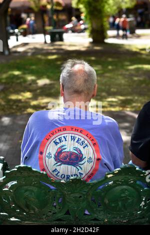 Un uomo che indossa una T-shirt ricordo Key West, Florida, si siede su una panchina del parco a Santa Fe, New Mexico. Foto Stock