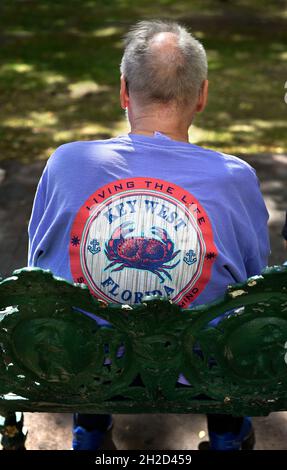 Un uomo che indossa una T-shirt ricordo Key West, Florida, si siede su una panchina del parco a Santa Fe, New Mexico. Foto Stock