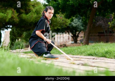 Donna che addestrano kung fu con un bastone in un parco Foto Stock