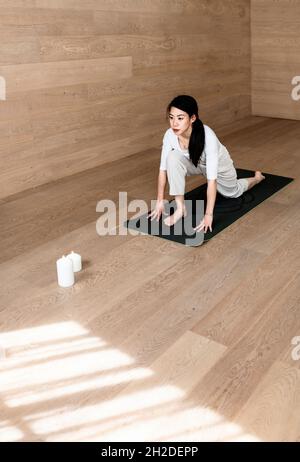 Giovane donna concentrata che fa gli esercizi di yoga mentre si siede sul pavimento Foto Stock