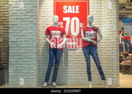 Due manichini femminili in T-shirt rosse e jeans blu in una vetrina contro uno sfondo di un muro di mattoni bianchi. Sconto promozionale del 70%. Bla Foto Stock