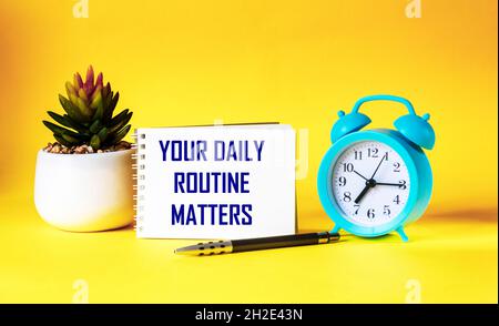 La vostra routine quotidiana. Scritto su un blocco note, accanto ad una sveglia, un cactus e una penna su sfondo giallo Foto Stock