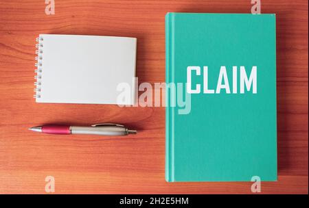 Rivendica, la parola è scritta su un blocco note verde e una tabella di legno, accanto ad un blocco note vuoto per la scrittura e una penna. Foto Stock