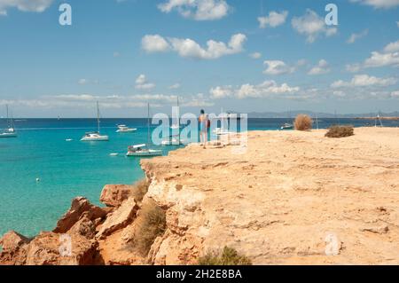 Un giovane turista guarda l'orizzonte sul Mar Mediterraneo dal bordo della costa rocciosa, sull'isola di Formentera in Spagna Foto Stock