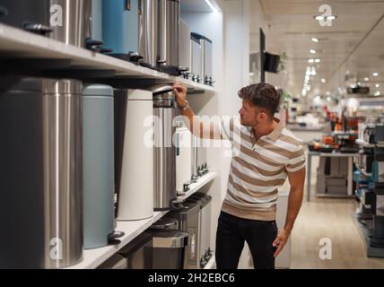 Cliente maschile in abiti casual apertura coperchio del moderno cestino posta su scaffale nel centro commerciale Foto Stock