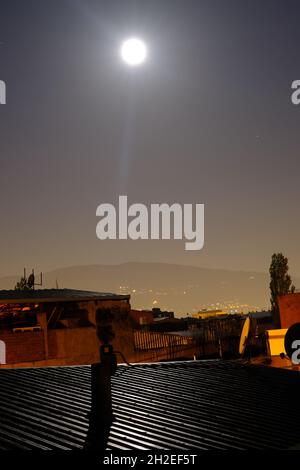 Luna piena nel mezzo della notte a Bursa, Luna e riflessione di luce sul tetto in metallo in ghetti a bursa con uludag e sfondo chiaro della città Foto Stock