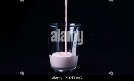 Primo piano di un bicchiere pulito riempito con frullato di fragola. Isolato su nero Foto Stock