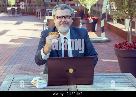 L'uomo finanziatore tiene soldi nelle sue mani e bitcoins. Ha fatto soldi con il suo laptop che commercia sulla borsa. Foto Stock