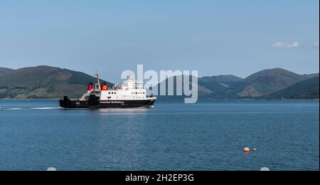 Traghetto per veicoli Calmac che lascia il porto di Rothesay lungo il tragitto per Wemyss Bay con Loch Striven e Cowal Peninsula sullo sfondo sotto un cielo blu chiaro. Foto Stock