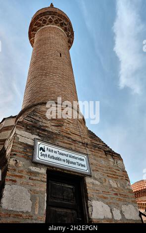 Nicaea (iznik), Bursa Turkey. Seyh kutbuddin e la sua tomba figlio fatto di mattoni rossi parete con il suo minareto si estende fino al cielo blu nuvoloso Foto Stock