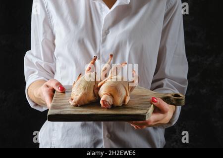 La donna inriconoscibile detiene due pernici crudi sul tagliere Foto Stock