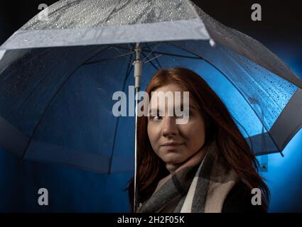 Ritratto di bella ragazza capelli rossi con occhi blu in piedi sotto ombrello trasparente di notte Foto Stock