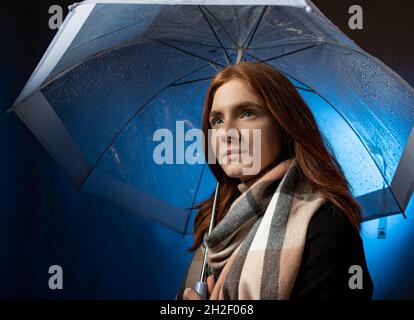 Ritratto di bella ragazza capelli rossi con occhi blu in piedi sotto ombrello trasparente di notte Foto Stock