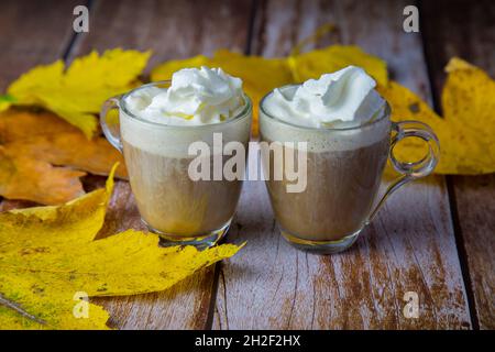 Due tazze di vetro con crema di caffè sul tavolo di legno decorato con foglie d'autunno gialle Foto Stock