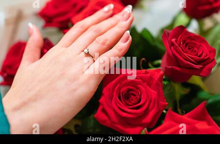 Mano femmina con anello di aggancio su un mazzo di rose rosse Foto Stock