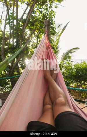 Le gambe dell'uomo in un'amaca durante l'ora d'oro vicino all'oceano Foto Stock