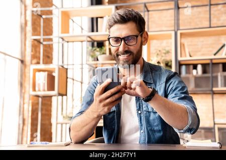 Ritratto di un uomo caucasico eccitato che utilizza lo smartphone mentre si riposa in ufficio Foto Stock