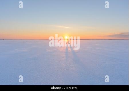 Donna con il suo cane in piedi su un ghiaccio di lago ghiacciato. Freddo giorno d'inverno, il sole tramonta all'orizzonte, Finlandia orientale. Foto Stock