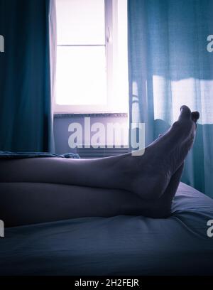 gambe femmine a letto all'ora blu Foto Stock