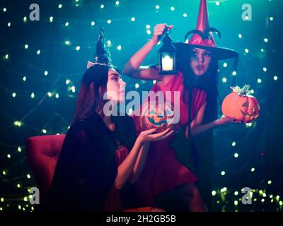 La giovane donna caucasica si siede mentre tiene la zucca scolpita in un volto con entrambe le mani. La sua amica in piedi con lanterna candela in Halloween party decora Foto Stock