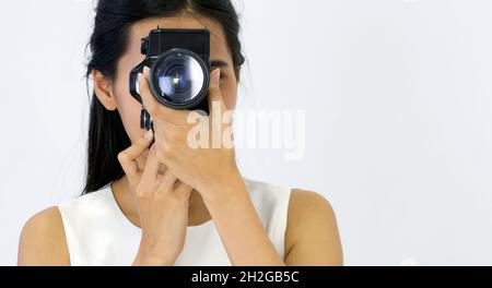 Giovane donna asiatica in abito bianco che guarda attraverso il mirino mentre scatti con la fotocamera. Foto Stock