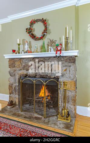 Accogliente camino in pietra di campo con fuoco e mantelpiece decorato per Natale con candele, decorazioni natalizie e una corona di vacanza. Foto Stock