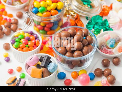Caramelle al cioccolato al latte in guscio con gomme da zucchero gelate e liquirizia e caramelle di sherbet di frutta su sfondo bianco. Con marshmallow e stra Foto Stock
