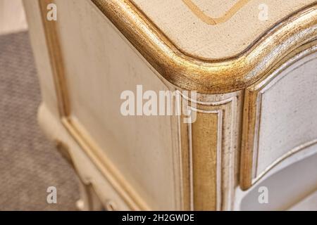 Elegante comodino in legno realizzato in stile classico con cassetti con decorazioni dorate lucide in camera luminosa vista ravvicinata Foto Stock