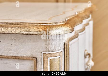 Elegante comodino in legno realizzato in stile classico con cassetti con decorazioni dorate lucide in camera luminosa vista ravvicinata Foto Stock