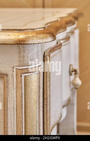 Elegante comodino in legno realizzato in stile classico con cassetti con decorazioni dorate lucide in camera luminosa vista ravvicinata Foto Stock