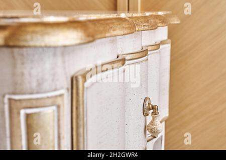 Elegante comodino in legno realizzato in stile classico con cassetti con decorazioni dorate lucide in camera luminosa vista ravvicinata Foto Stock