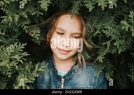 ritratto del volto di una bella caucasica caucasica candida sana bambina di otto anni circondato da rami e foglie di verde thuja pianta o cypres Foto Stock