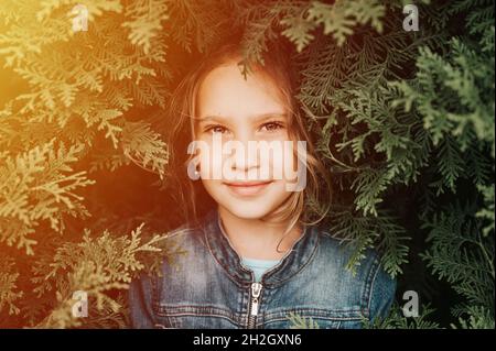 ritratto del volto di una bella caucasica caucasica candida sana bambina di otto anni circondato da rami e foglie di verde thuja pianta o cypres Foto Stock