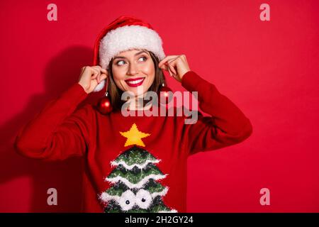 Foto di dolce cute giovane donna vestita stampa pullover tenuta decorazioni natalizie cercando spazio vuoto isolato colore rosso sfondo. Foto Stock