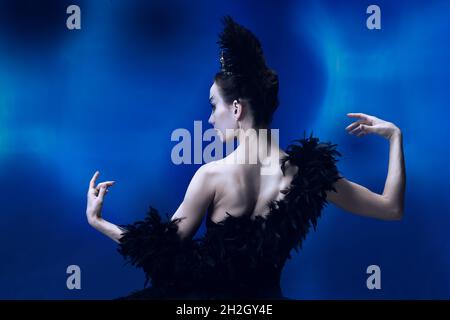 Vista posteriore di bella donna, ballerina flessibile in abito balletto nero, tutu ballare in studio blu pieno di luce. Foto Stock
