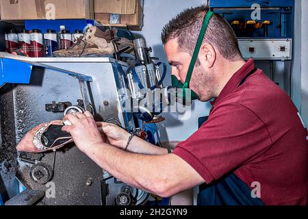 Giovane calzolaio che menda le calzature in officina. Foto Stock