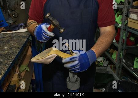 Giovane calzolaio che menda le calzature in officina. Foto Stock