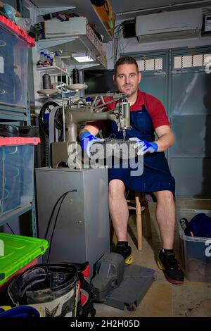 Giovane calzolaio che menda le calzature in officina. Foto Stock
