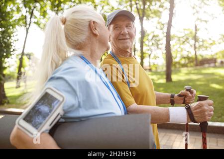 Uomo anziano allegro con pali per nordic walking e donna nel parco verde Foto Stock