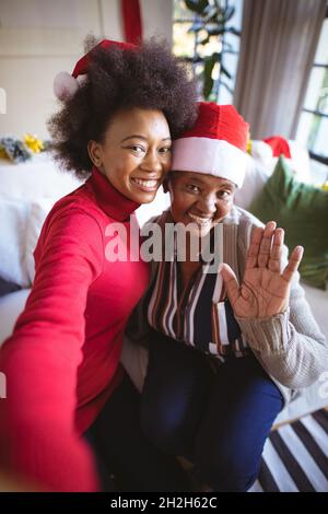 Sorridente afroamericana figlia adulto e madre anziana in cappelli di santa prendendo selfie di natale Foto Stock