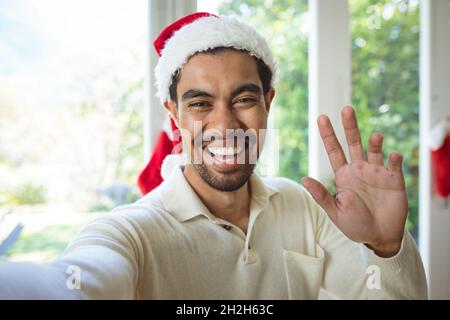 Ritratto di felice uomo biraciale in santa Hat fare videochiamata di natale Foto Stock