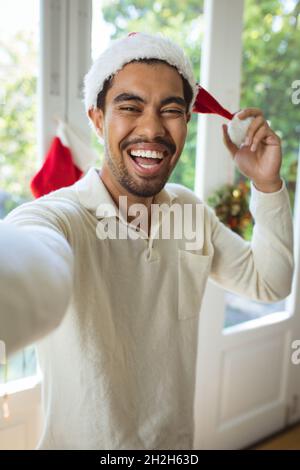 Ritratto di felice uomo biraciale in santa Hat fare videochiamata di natale Foto Stock