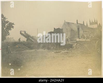 St Marys Church, Church Street, Littlehampton, Arun, West Sussex, 1901-1902. Persone al lavoro che utilizzano una macchina trebbiatrice a vapore, con la Chiesa di Santa Maria sullo sfondo. Fotografato come parte di una serie che registra le opere di Holborn e Strand Improvement. La Chiesa di Santa Maria fu estesa verso est verso la fine del XIX secolo, con un nuovo coro e la Cappella della Signora, tuttavia entro il 1930 la condizione strutturale della chiesa era così brutta che doveva essere demolita. Questa fotografia mostra l'edificio con l'estensione del tardo 19 ° secolo. Foto Stock