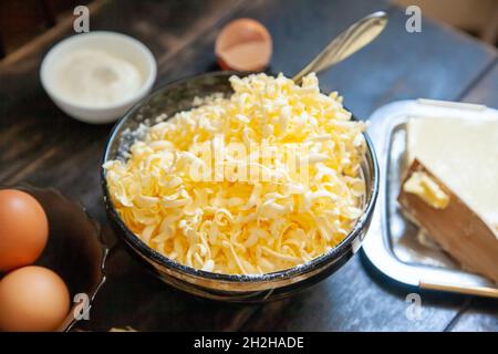 Burro grattugiato per la cottura. Ingredienti di cottura per pasticceria frolla: Burro, uova, panna acida su tavola di legno. Foto Stock