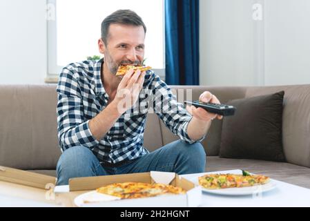Uomo che guarda la TV mentre si mangia la pizza. Trascorrere del tempo libero a casa Foto Stock